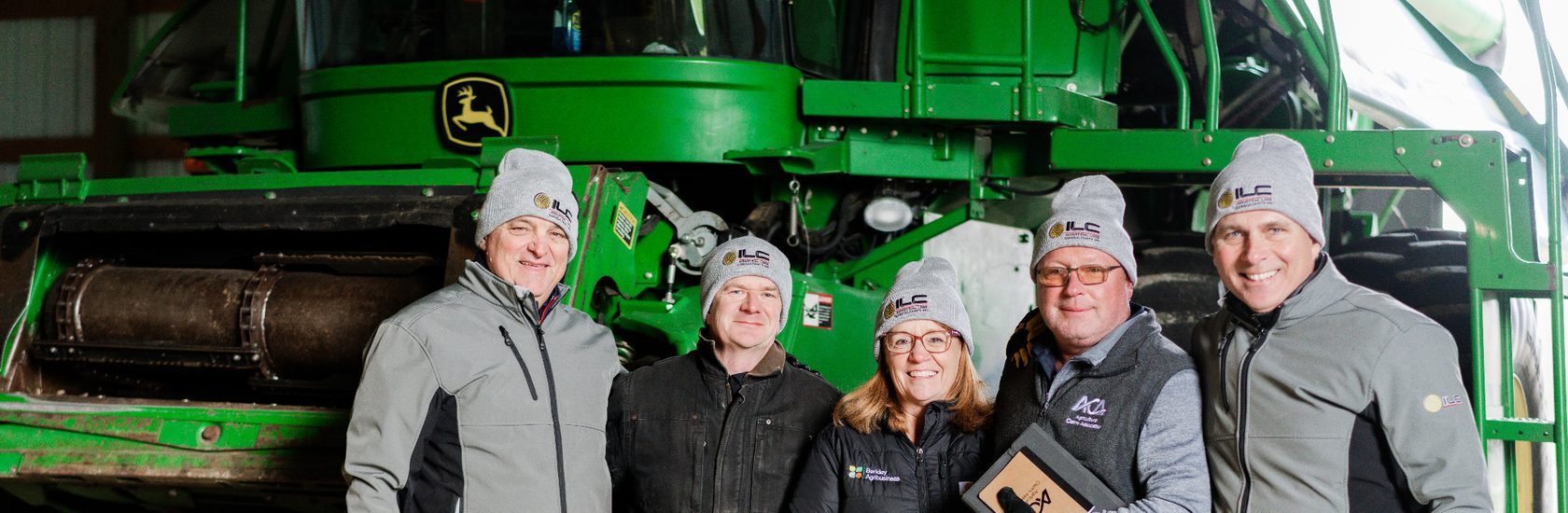 Industrial Loss Consultants team posing in front of large agricultural machinery during an industry event, showcasing hands-on expertise in agricultural equipment, machinery and equipment consulting, and loss investigation.