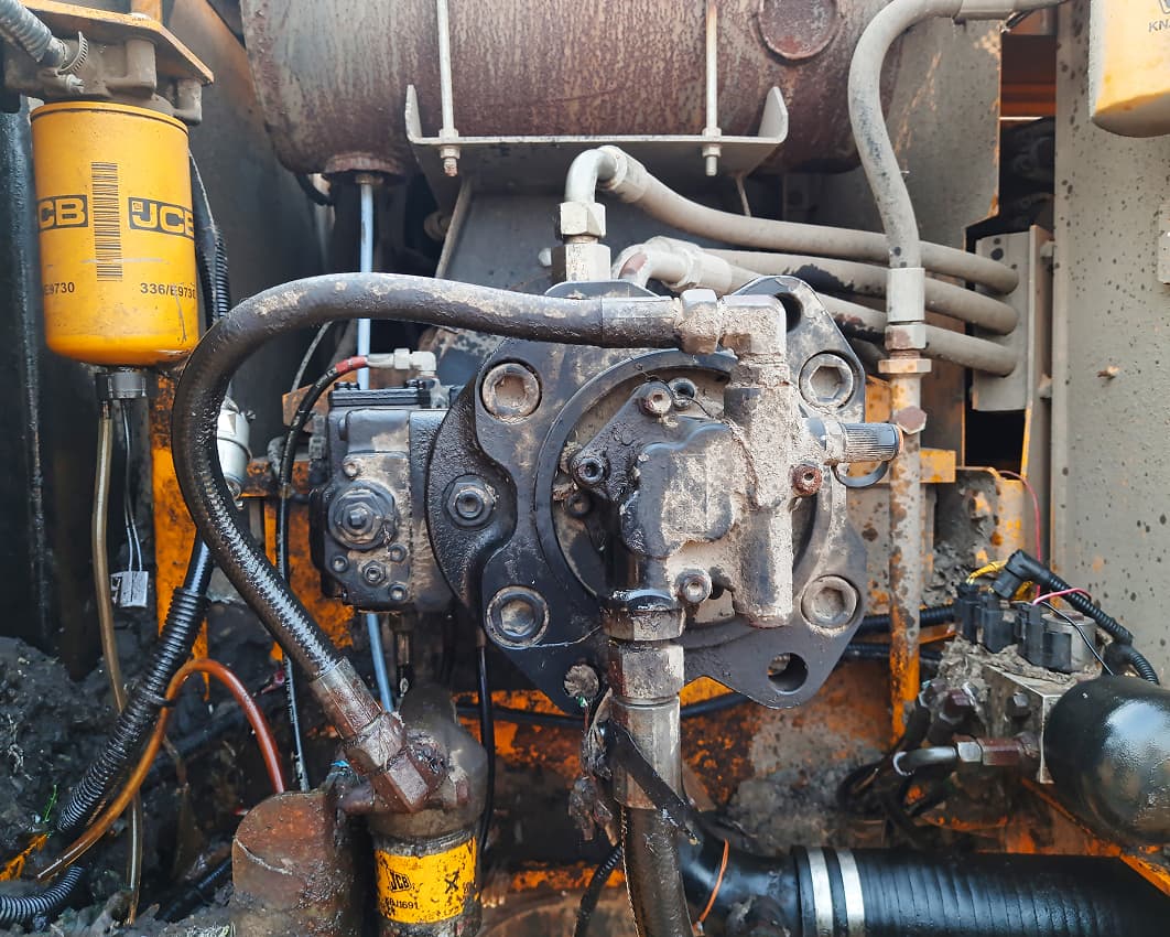 Close-up view of a dirty, yellow industrial machine engine with various pipes, cables, and components, including a JCB oil filter on the left and signs of oil leaks and wear.
