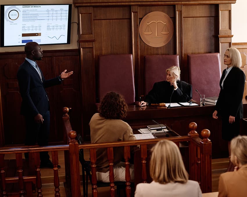 A man delivers a presentation in a courtroom, while a group of people listens intently from their seats.